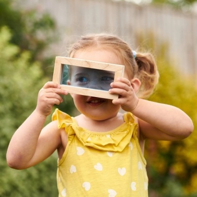 Criança com vestido amarelo segurando espelho com moldura de madeira