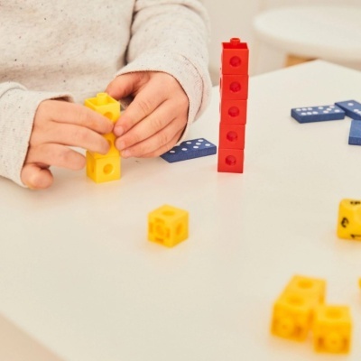 Criança a montar blocos de construção amarelos e vermelhos sobre mesa branca