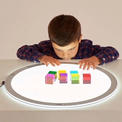 Criança a observar cubos coloridos sobre superfície luminosa circular.