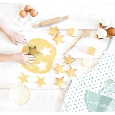 Mãos a cortar massa com cortador de estrelas na mesa com utensílios e confeitos