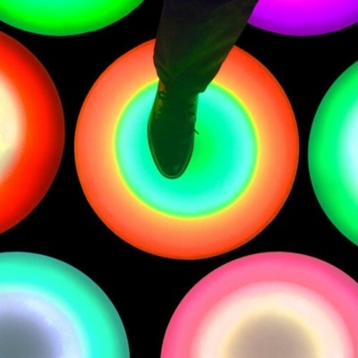 Círculos luminosos coloridos no chão com pé calçado a pisar num deles