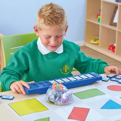 Criança com camisola verde a jogar com peças numeradas e tabuleiro azul numa mesa branca e colorida em ambiente escolar
