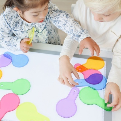 Crianças brincando com raquetes coloridas de plástico translúcido sobre mesa branca
