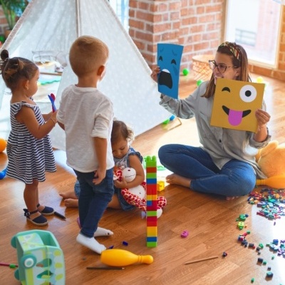 Mulher e crianças a brincar com cartões de emojis e brinquedos num chão de madeira