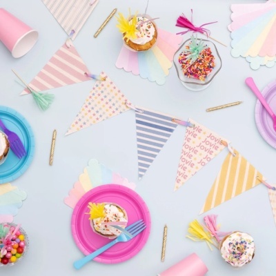 Mesa decorada para festa com cupcakes, pratos, copos, guardanapos, bandeirolas e velas douradas