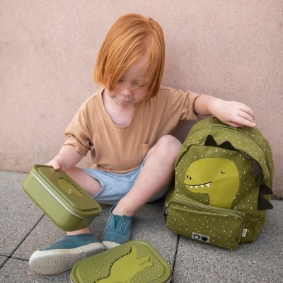 Criança com mochila e caixas de almoço verdes com dinossauros sentada no chão