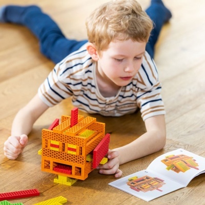 Menino a construir modelo com peças coloridas de plástico no chão