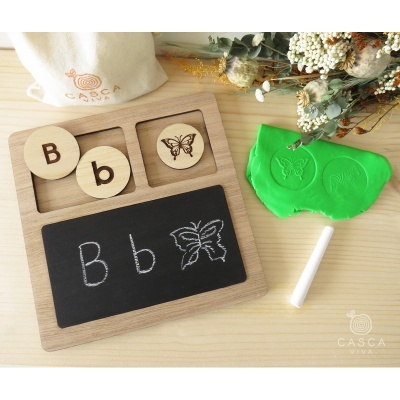 Painel educativo de madeira com letras e desenhos de borboleta, giz branco e massa de modelar verde com carimbos