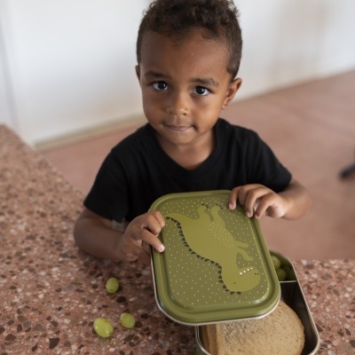 Caixa de lanche verde com desenho de crocodilo e sanduíche, com criança segurando a tampa