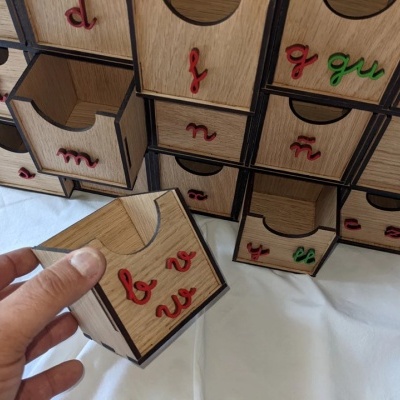 Caixas pequenas de madeira com gavetas numeradas com letras minúsculas coloridas