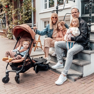 Carrinho de bebé castanho com bebé e família sentada nos degraus de casa