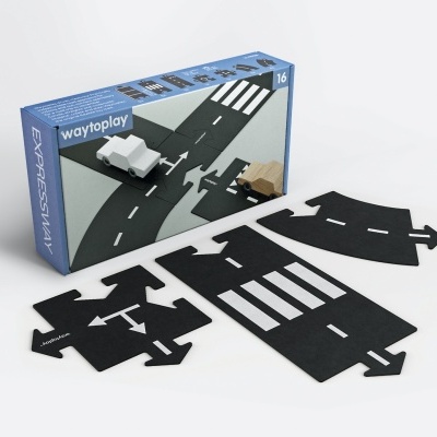 Peças de estrada tipo puzzle pretas com linhas brancas para montar circuitos e dois pequenos veículos, ao lado de caixa azul.