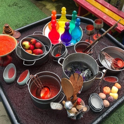 Utensílios de cozinha coloridos e metálicos num tabuleiro preto ao ar livre