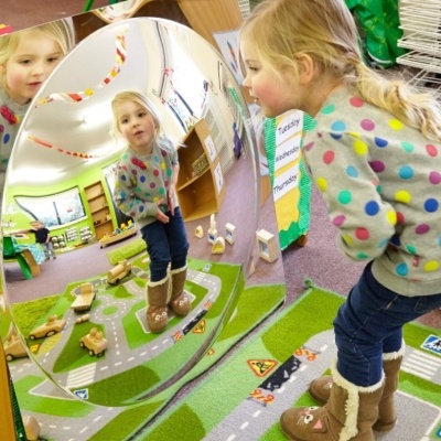 Espelho convexo refletindo criança num ambiente colorido com tapete de estrada e brinquedos.