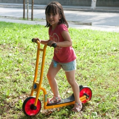 Criança num trotinete amarelo com rodas vermelhas num parque com relva verde
