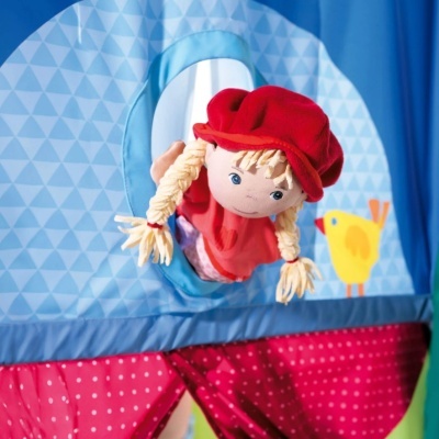 Tenda infantil azul com boneca de pano a sair pela janela e painel vermelho com bolinhas brancas.