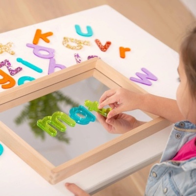 Espelho quadrado de madeira com letras coloridas e mão de criança a brincar