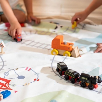 Tapete de jogo com trilhos e brinquedos de comboio em madeira com crianças a brincar