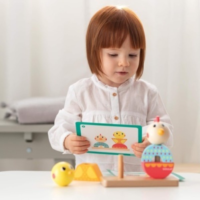 Criança de camisa branca a brincar com brinquedos coloridos de madeira