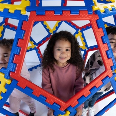 Crianças brincam dentro de estrutura geométrica feita de peças de plástico coloridas
