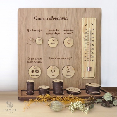 Painel de madeira com discos móveis e termómetro, texto em português, sobre mesa com decoração natural