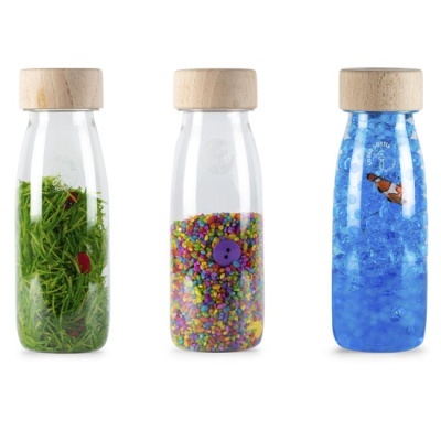 Três garrafas transparentes com tampa em madeira contendo ervas verdes, bolinhas coloridas com botão roxo e esferas azuis com peixe.