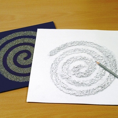 Dois pedaços de papel quadrados com padrão espiral, um branco com lápis cinza e um azul escuro, sobre uma superfície de madeira.