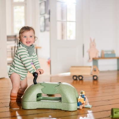 Criança com fralda riscada e meias brinca com brinquedo verde dentro de casa
