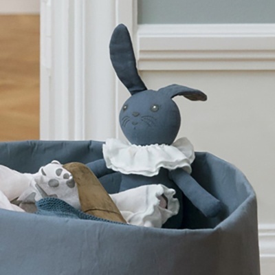 Ursinho de peluche azul escuro com babado branco numa cesta azul em tecido