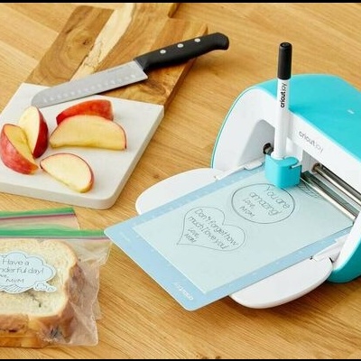 Máquina de corte e escrita de papel azul e branco a cortar cartolina azul numa mesa de madeira