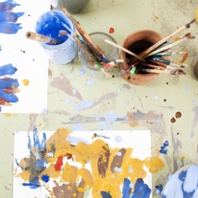 Mesa com tintas, pincéis em recipientes e folhas com pinturas multicoloridas