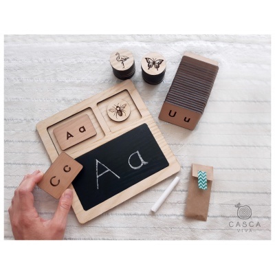 Material educativo em madeira com letras gravadas, desenhos de animais e ardósia para escrita com giz.