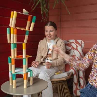 Blocos de madeira coloridos empilhados em torre com criança e adulto ao fundo