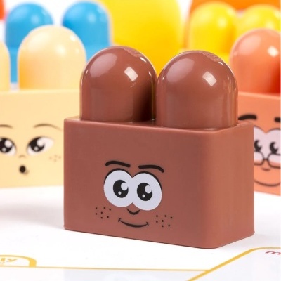 Bloco de construção castanho com rosto expressivo e dois pinos, com outros blocos coloridos ao fundo