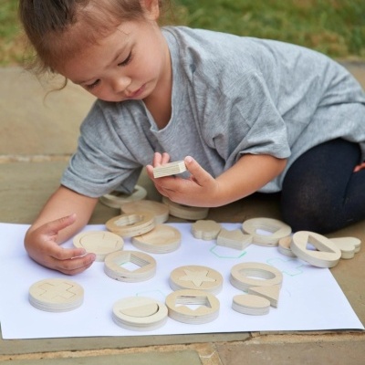Criança brincando com peças de madeira em formas geométricas sobre uma folha branca.