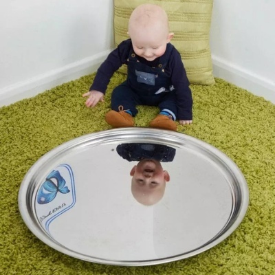 Criança sentada em tapete verde com espelho refletindo o seu rosto