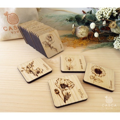 Cartões de madeira com gravuras de flores e nomes em português sobre mesa de madeira clara