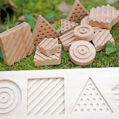 Brinquedos de madeira com formas geométricas e texturas diferentes sobre musgo