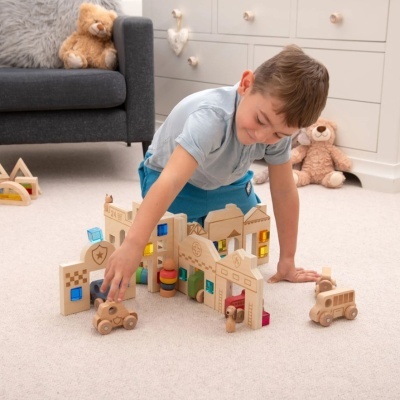 Criança a brincar com brinquedos de madeira numa sala com sofá e peluches.