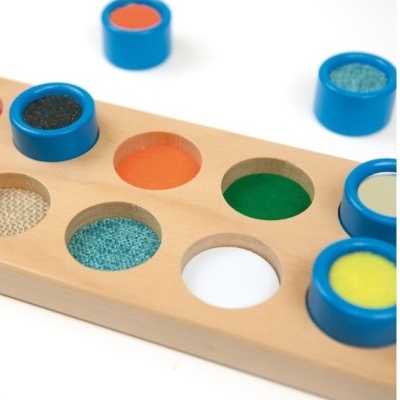 Tabuleiro de madeira com recortes circulares coloridos e texturizados e peças azuis encaixáveis