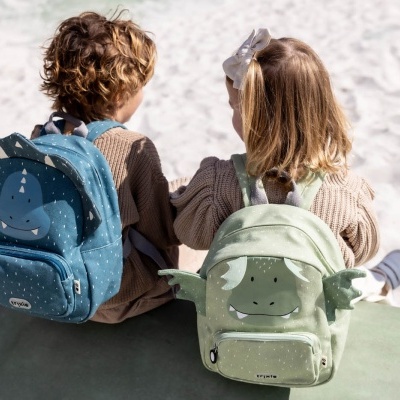 Crianças com mochilas azuis e verdes sentadas sobre superfície verde em ambiente arenoso.