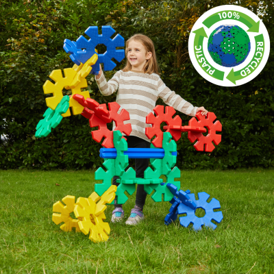 Menina a montar grande estrutura colorida de peças plásticas em jardim com selo de reciclagem