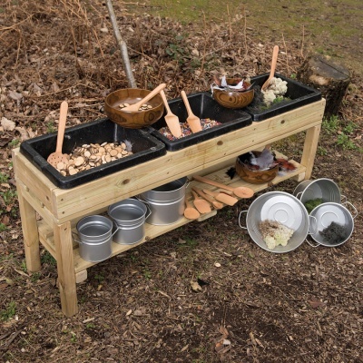 Banco de madeira com cubetas pretas e utensílios de jardinagem infantis em zona exterior