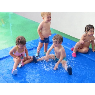 Crianças pequenas a brincar na água sobre um tapete azul molhado