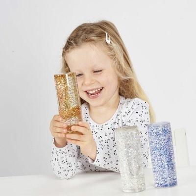 Criança a segurar tubo com purpurina dourada, com tubos prateado e azul na mesa branca