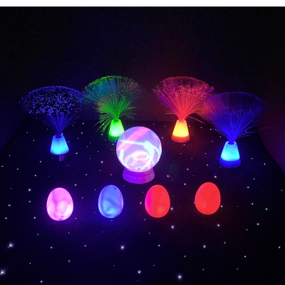 Conjunto de luzes decorativas coloridas em fibra ótica e lâmpadas luminosas sobre fundo preto com pontos de luz branca.