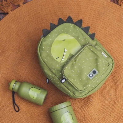 Mochila verde de dinossauro com garrafa e recipiente térmico verdes em tapete laranja redondo