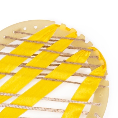 Objeto circular bege com tiras amarelas entrelaçadas com cordas em fundo branco