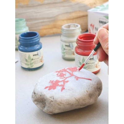 Três frascos de tinta acrílica e mão pintando pedra cinza com tinta vermelha