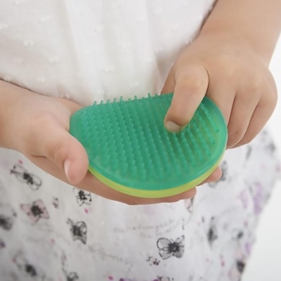 Criança segurando escova de silicone verde com cerdas flexíveis.